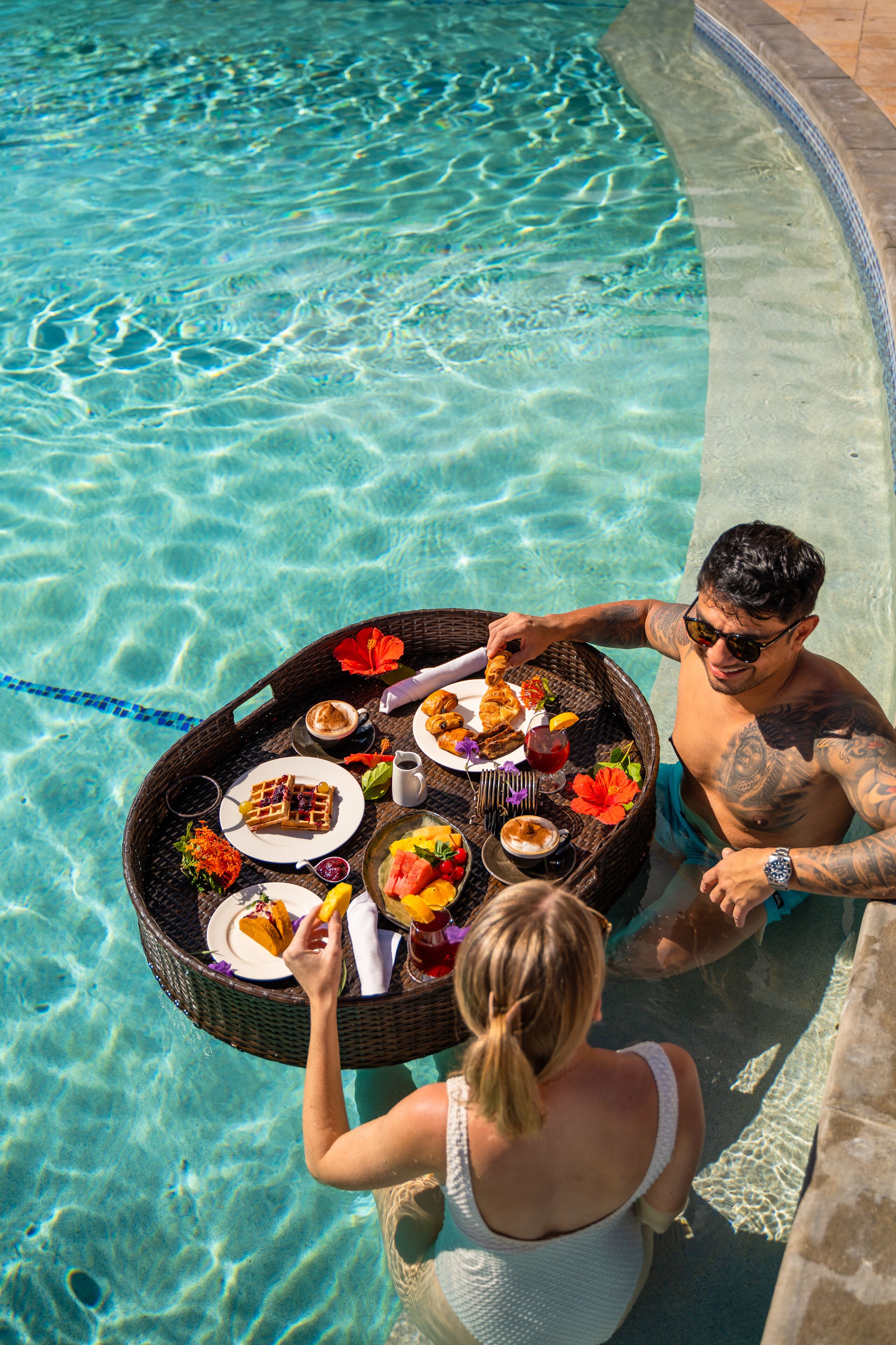 A dining table with food and drinks by a poolside.