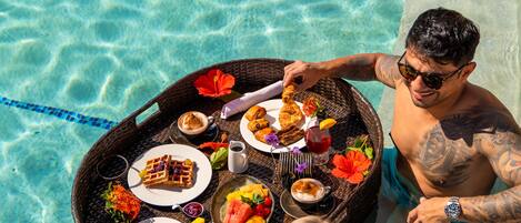 A dining table with food and drinks by a poolside.