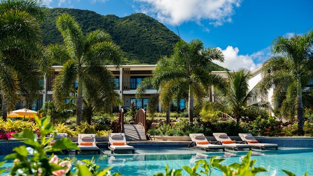 A pool area with lounge chairs, a wooden bridge, and a mountain backdrop.