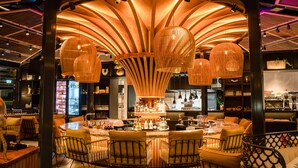 A bar area with a central round table, multiple hanging light fixtures, and a variety of bottles and glasses on shelves.