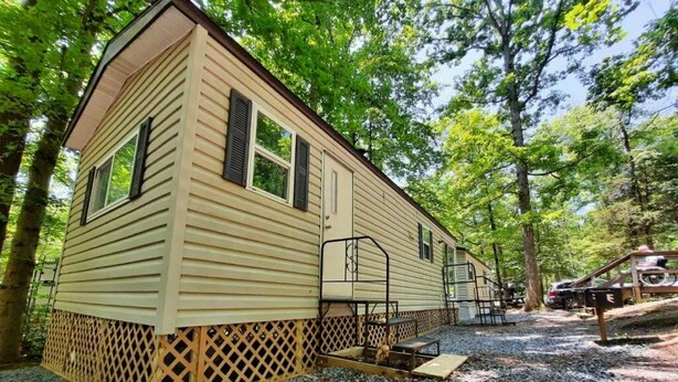 Une maison mobile de plain-pied, posée sur une fondation en treillis, avec un petit porche et une allée gravillonnée.