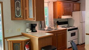 Une cuisine compacte dotée d’armoires en bois, d’une cuisinière, d’un réfrigérateur, d’une machine à café et d’une poubelle.