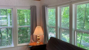 Une pièce dotée d’un ventilateur de plafond, d’un climatiseur, d’un canapé, d’une lampe et de grandes fenêtres avec des rideaux.