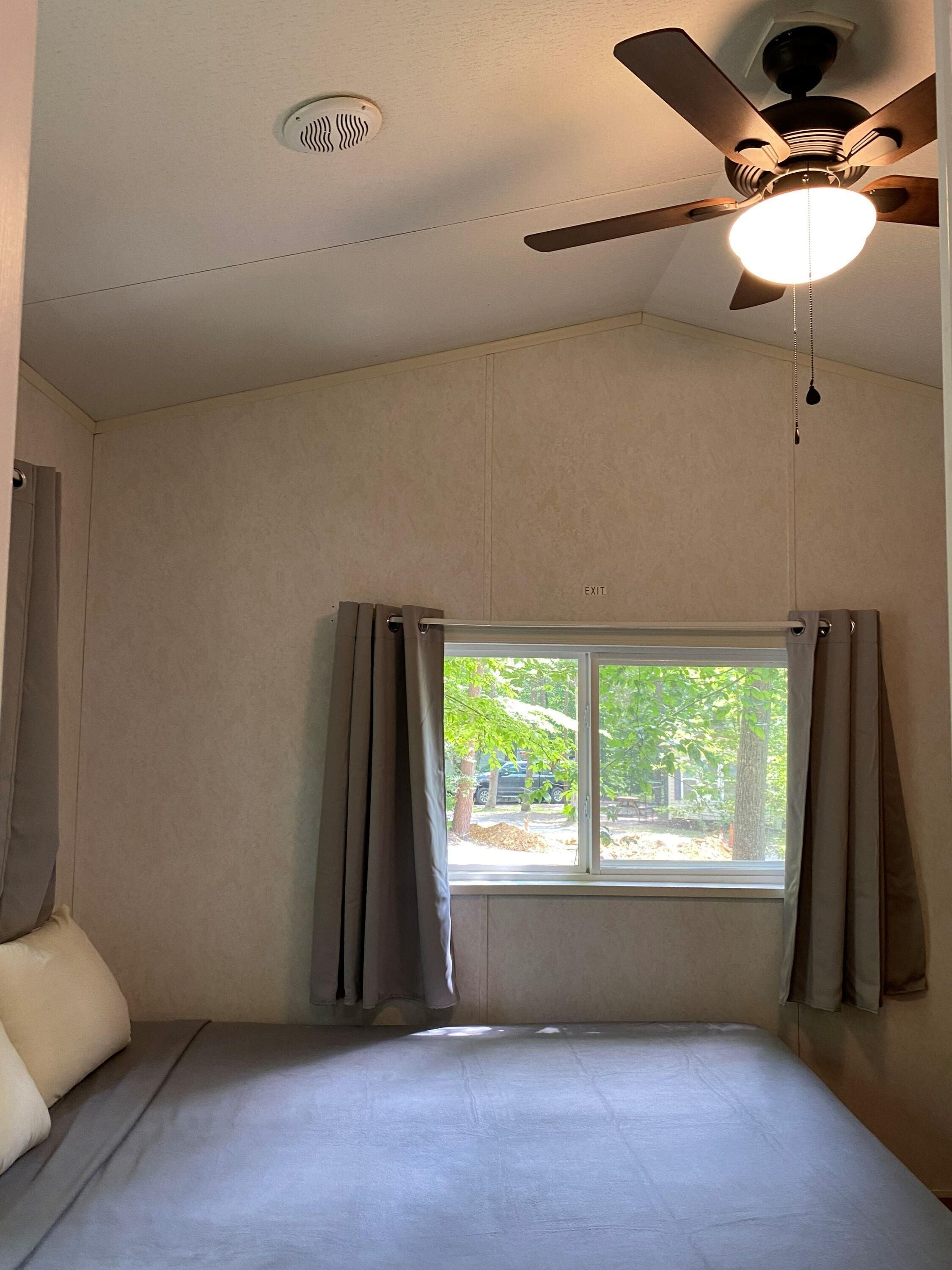 Un dormitorio con una cama individual, un ventilador de techo, una ventana con cortinas y una señal de salida.