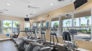 A gym with various exercise equipment, large windows with views of palm trees, and a ceiling fan. - Magical Location Condo Close to Clubhouse & Pool - Windsor Hill Resort (Kissimmee)