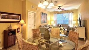 A dining area with a glass-top table surrounded by wicker chairs, a ceiling fan, and a chandelier. - Magical Location Condo Close to Clubhouse & Pool - Windsor Hill Resort (Kissimmee)