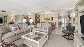 A spacious living room with a sofa, armchairs, a coffee table, and a dining area in the background.