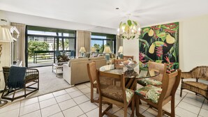 A spacious living room with a dining area, large windows, and a tropical-themed painting.
