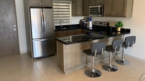 A modern kitchen with stainless steel appliances, a central island with bar stools, and wooden cabinets. - Amazing penthouse close to the beach (Cabo San Lucas)