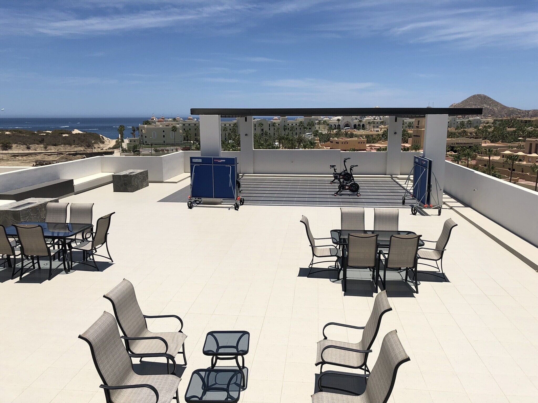 A rooftop terrace with outdoor seating, a covered area, and a view of the sea and distant buildings.