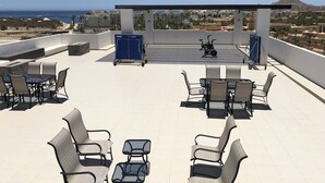 A rooftop terrace with outdoor seating, a covered area, and a view of the sea and distant buildings. - Amazing penthouse close to the beach (Cabo San Lucas)
