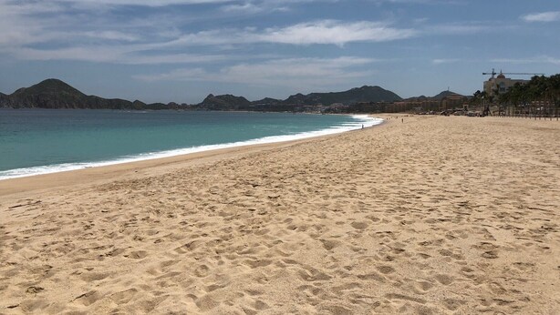 A wide sandy beach with clear blue water and distant mountains. - Amazing penthouse close to the beach (Cabo San Lucas)