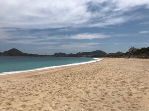 Ein weiter Sandstrand mit klarem, blauen Wasser und fernen Bergen.