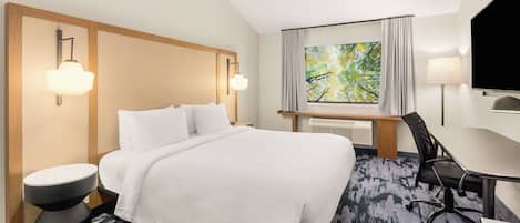Une chambre d’hôtel équipée d’un lit, d’un bureau, d’une chaise, d’une télévision et d’une fenêtre donnant sur la verdure.