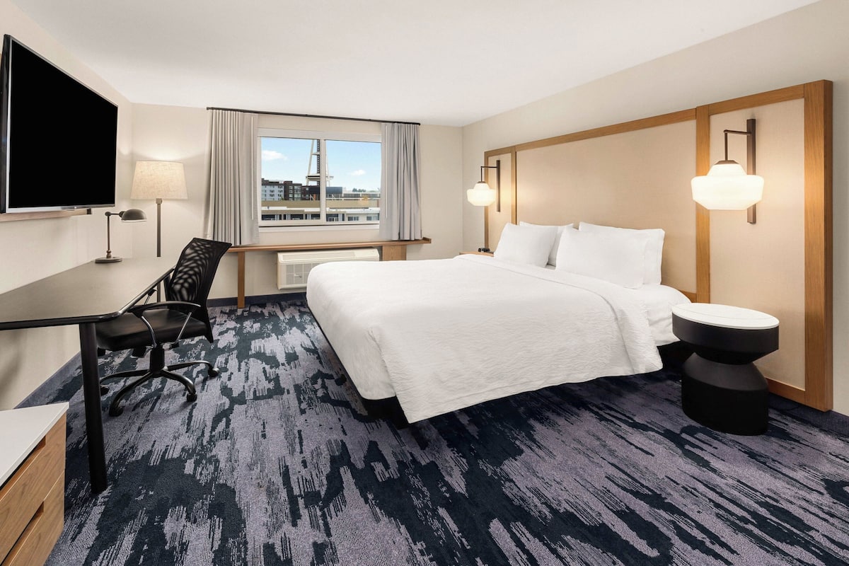 A hotel room with a large bed, a desk, a chair, a TV, and a window with curtains.