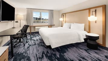 Ein Hotelzimmer mit einem großen Bett, einem Schreibtisch, einem Sessel, einem Fernseher und einem Fenster mit Vorhängen.