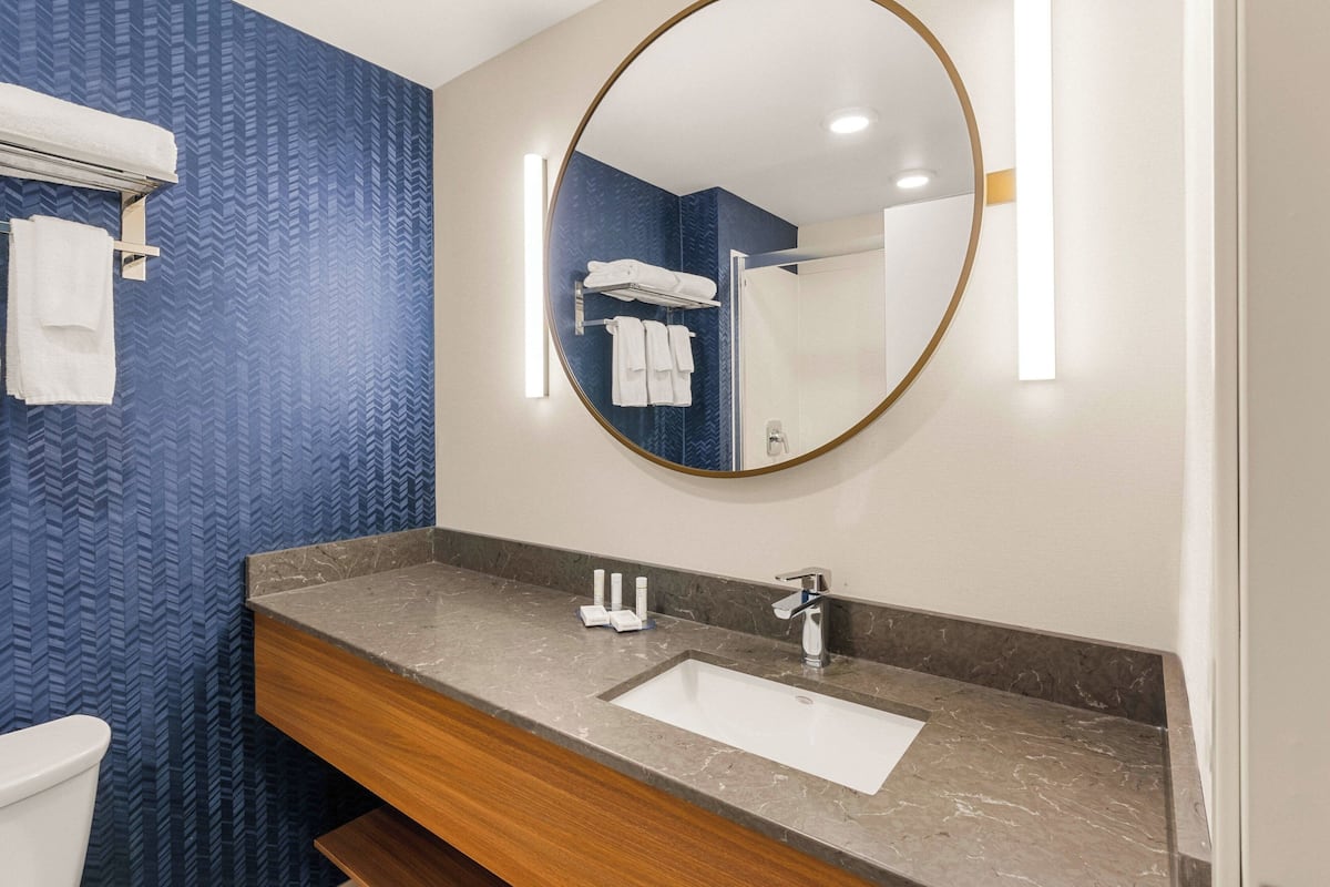 A bathroom with a marble sink, a wooden vanity, a large mirror, and towels on a rack.