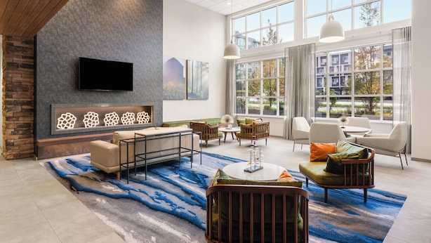A spacious living area with a stone accent wall, a flat-screen TV, and a large window offering a view of buildings and trees. - Fairfield Inn & Suites by Marriott Seattle Downtown/Seattle Center (Seattle)