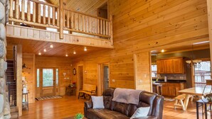 Ein geräumiges Blockhaus-Interieur mit Holzbalkendecke, einem Balkon, einem Wohnzimmer mit Ledersofa, einem Essbereich und einer Küche.