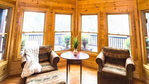 Ein Zimmer mit hohen Decken und Holzboden, ausgestattet mit großen Fenstern, zwei Sesseln, einem kleinen Tisch und einem Blumentopf.