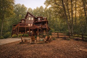 Una cabaña de madera grande con varios balcones y una terraza, rodeada de un bosque.