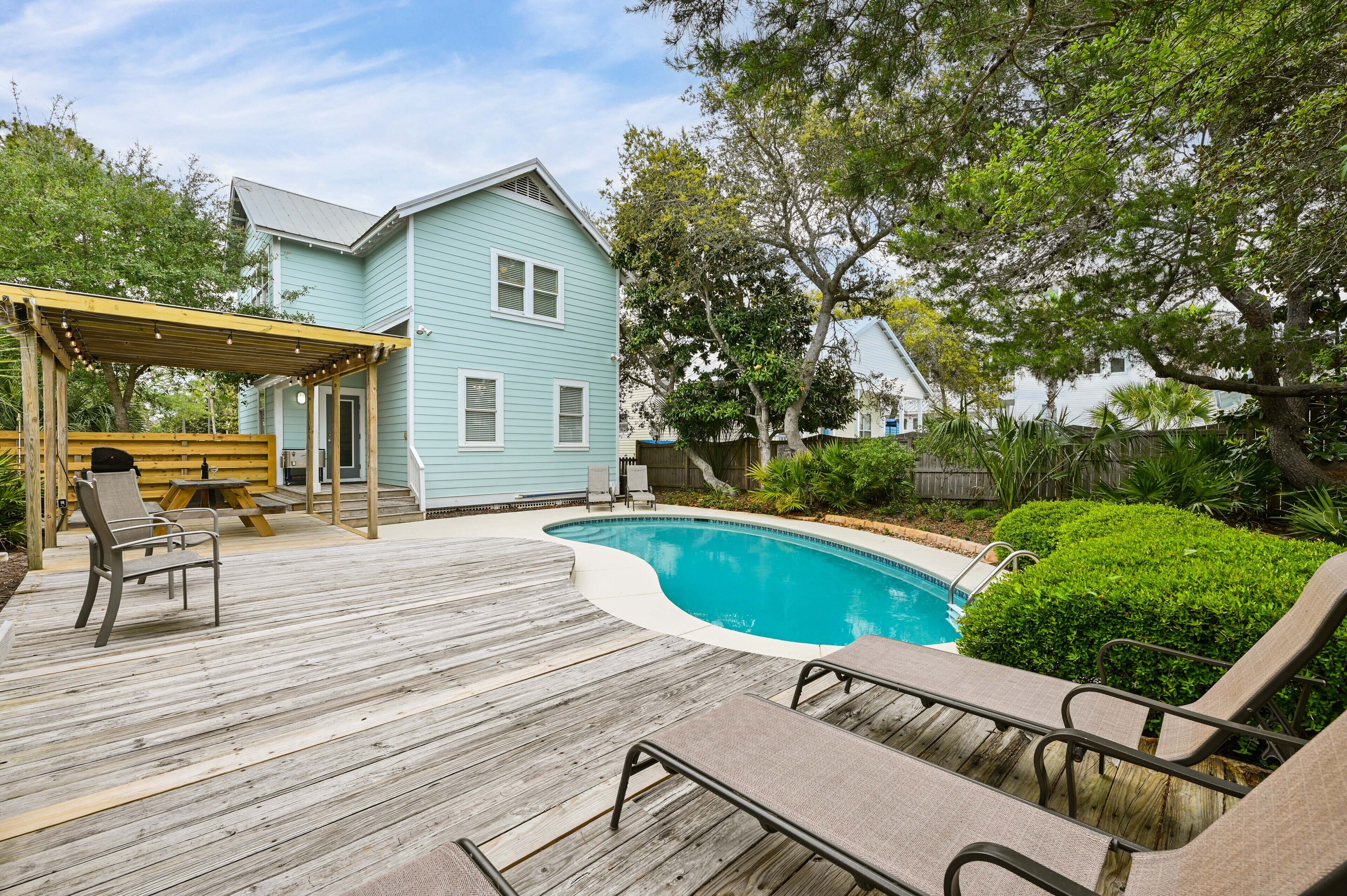 A backyard with a swimming pool, wooden deck, and outdoor seating.