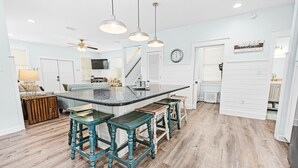 Cucina con isola centrale, sgabelli da bar, pavimento in legno, lampade a sospensione e ventilatore a soffitto.