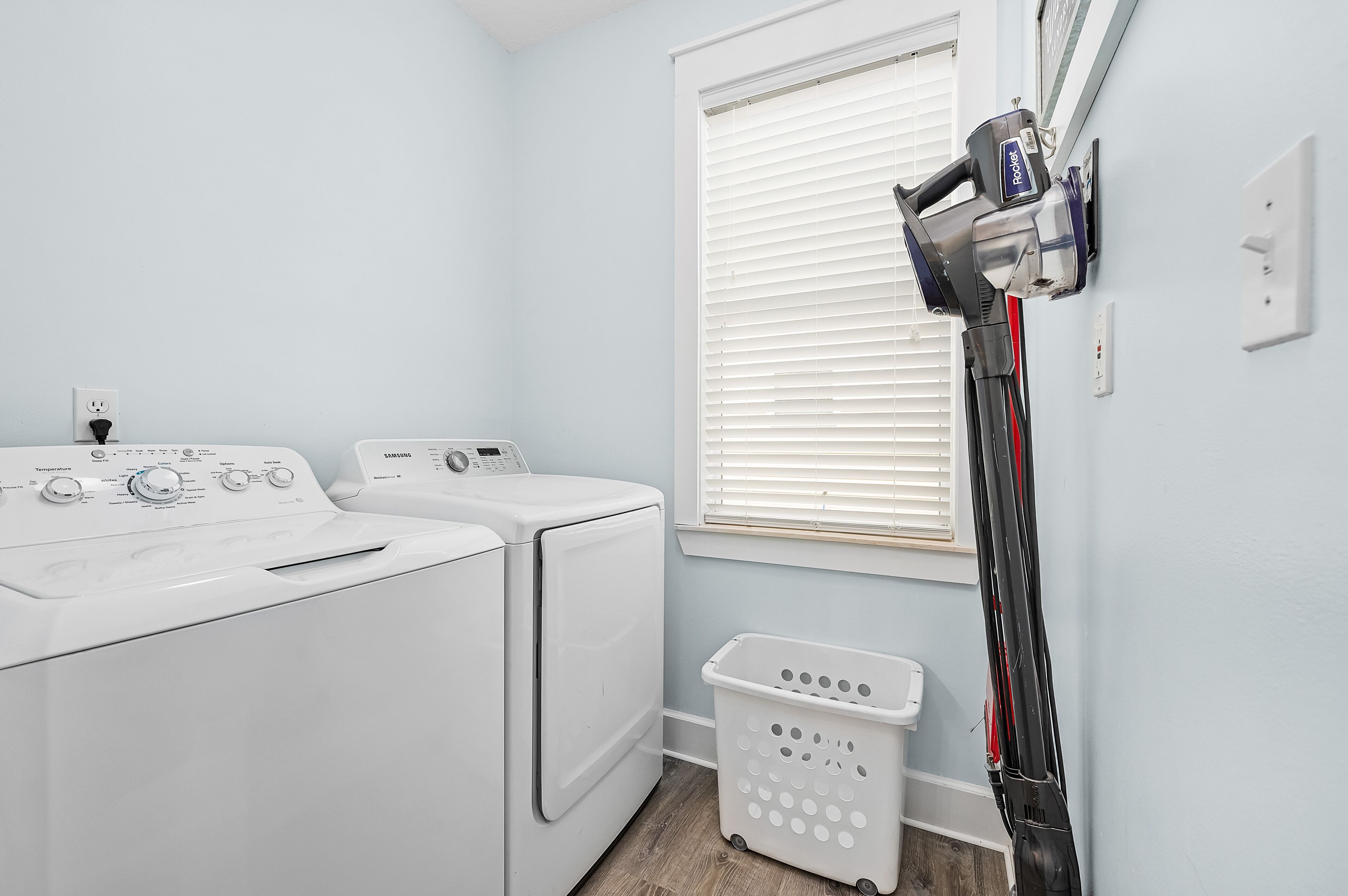 A laundry room with two white front-loading washing machines, a wall-mounted steam iron, and a laundry basket.
