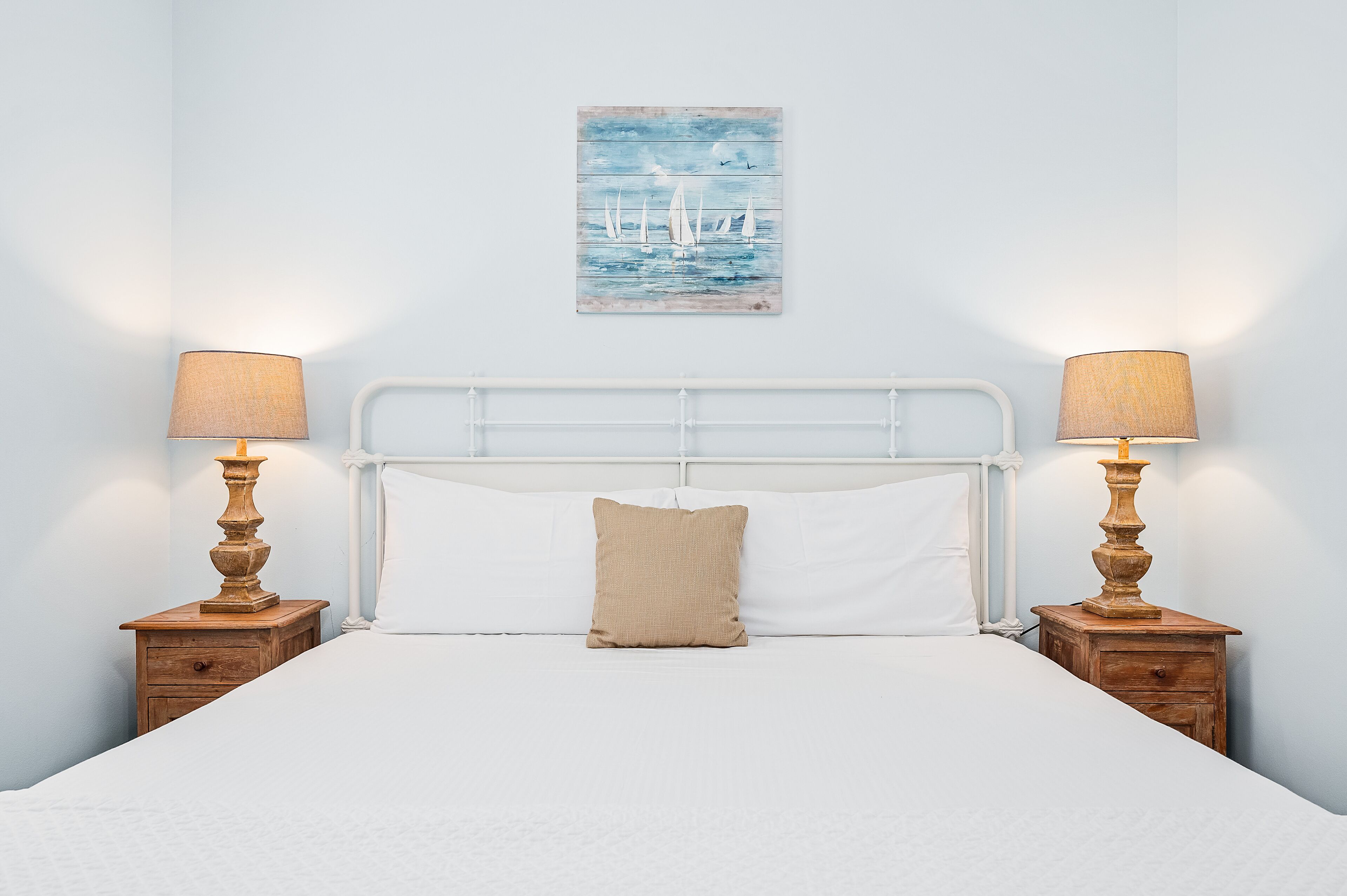 A neatly made bed with white linens, a beige pillow, and two bedside tables with lamps.
