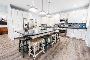 Une cuisine moderne avec des meubles blancs, un îlot central, des tabourets de bar et des appareils électroménagers en acier inoxydable.