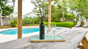 Un tavolo di legno con una bottiglia e due bicchieri su un vassoio, vicino a una piscina.
