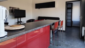 Eine moderne Küche mit einer roten Kochinsel, schwarzen Schränken und einem an der Wand montierten Flachbildfernseher.