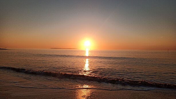 Ein Sonnenuntergang über einem ruhigen Meer mit einer entfernten Küstenlinie.
