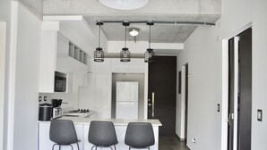 Una cocina moderna con armarios blancos, una isla central con taburetes altos y lámparas colgantes.