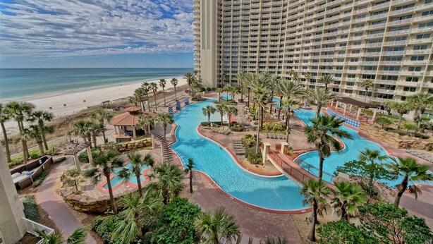 A hotel with a large pool area, palm trees, and a beach view.