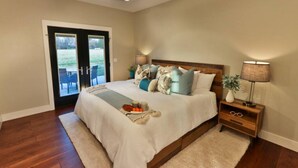 A bedroom with a bed, bedside tables, a lamp, and a view through a door.