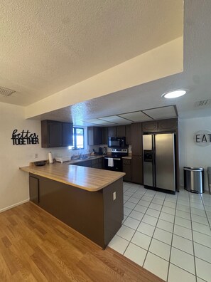 Een moderne keuken met een centraal eiland, roestvrijstalen apparatuur en een bord met de tekst 'beter samen' aan de muur.