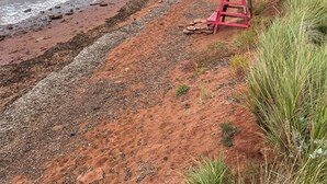 A beach with red chairs and a rocky shoreline. - The Homestead, in Bedeque, waterview beach house and hot tub cabin (Bedeque)