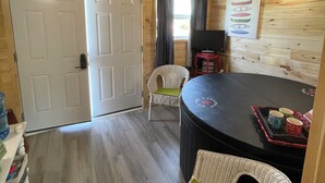 A cozy cabin interior with a dining table, wicker chairs, a television, and a sign on the wall. - The Homestead, in Bedeque, waterview beach house and hot tub cabin (Bedeque)