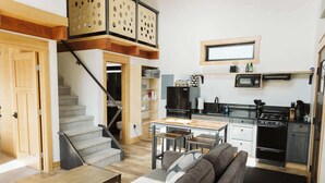 A compact living space with a staircase leading to a loft, a kitchenette, and a seating area with a sofa and table. - Steelhead cabin @ Keystone Kozy (Soldotna)