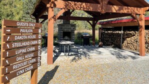 A wooden pavilion with a stone fireplace and a signpost indicating various cabins and a pavilion. - Steelhead cabin @ Keystone Kozy (Soldotna)