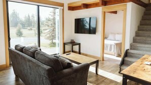 A modern living room with a sofa, a coffee table, a TV, and a staircase leading to a bedroom. - Steelhead cabin @ Keystone Kozy (Soldotna)