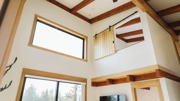 A multi-level interior with large windows, wooden beams, and a staircase. - Steelhead cabin @ Keystone Kozy (Soldotna)