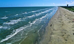 A beach with waves, a sandy shore, and a tower in the distance.