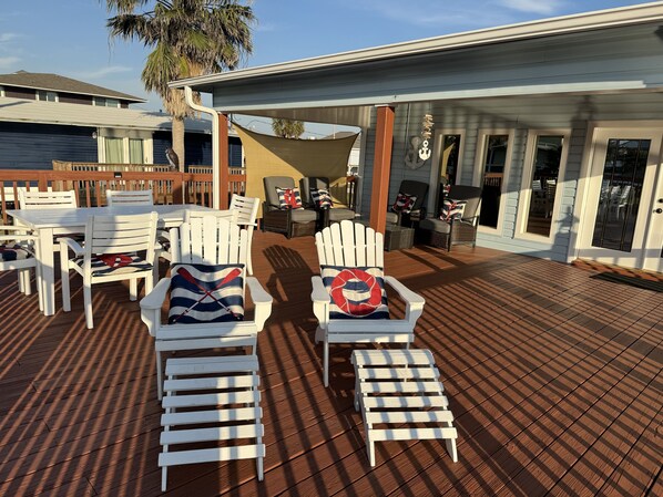 A deck with white Adirondack chairs, a small table, and a lounge chair.