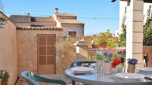 En terrasse med et bord dækket til to, omgivet af stenvægge og krukker med planter.