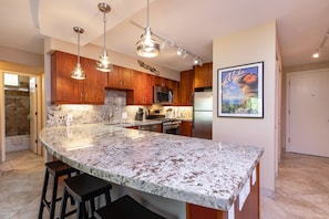 A kitchen with granite countertops, wooden cabinets, stainless steel appliances, and pendant lighting.