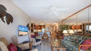 Amplia sala de estar con muebles de mimbre, una mesa de centro de cristal y vista a la cocina al fondo.
