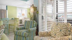 A bright kitchen with white cabinets, a dining table with chairs, and a window with blinds.