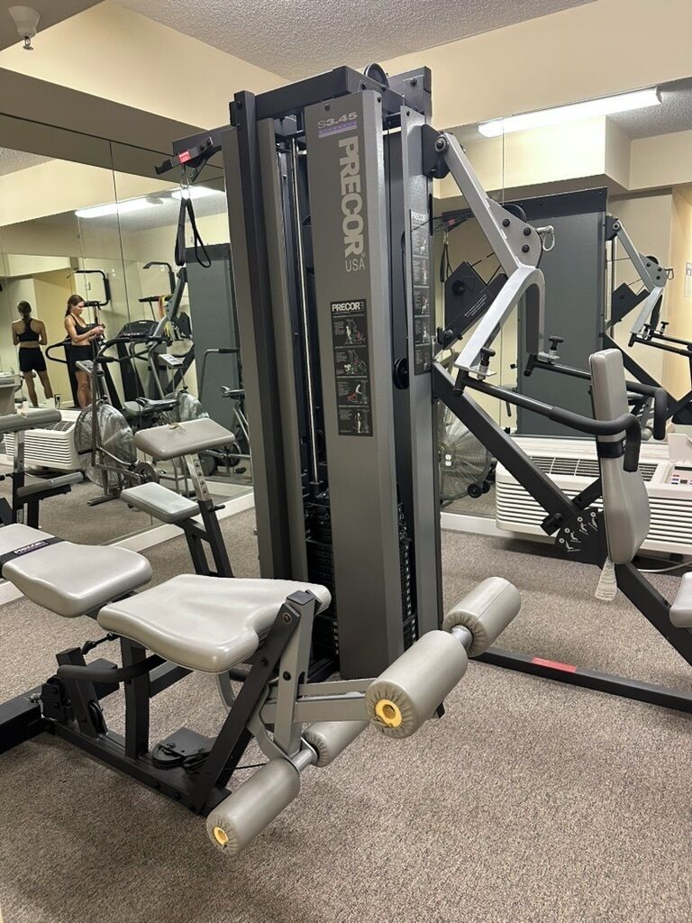 Un gimnasio con equipo de ejercicio, incluyendo una jaula de sentadillas y bancos de pesas.